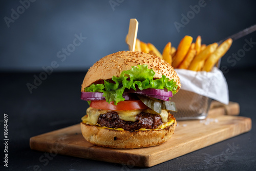 Tasty grilled beef burger with lettuce, cheese and onion served on cutting board on a black wooden table, with copyspace.