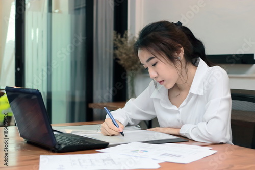 Attractive young Asian business woman working with laptop computer on the workplace in office.