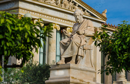 Statue of the great Greek philosopher Plato sitting on a marble chair, background of classical Greek columns.