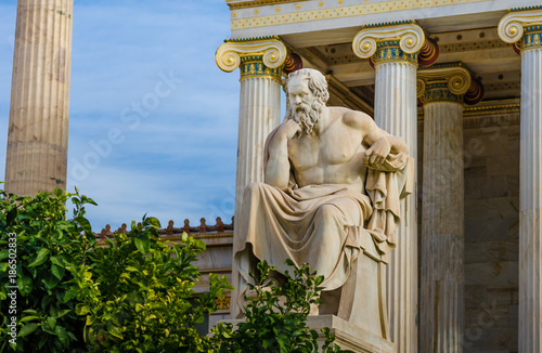 Statue of the greatest Greek philosopher Socrates sitting on a marble chair, background of classical Greek columns.