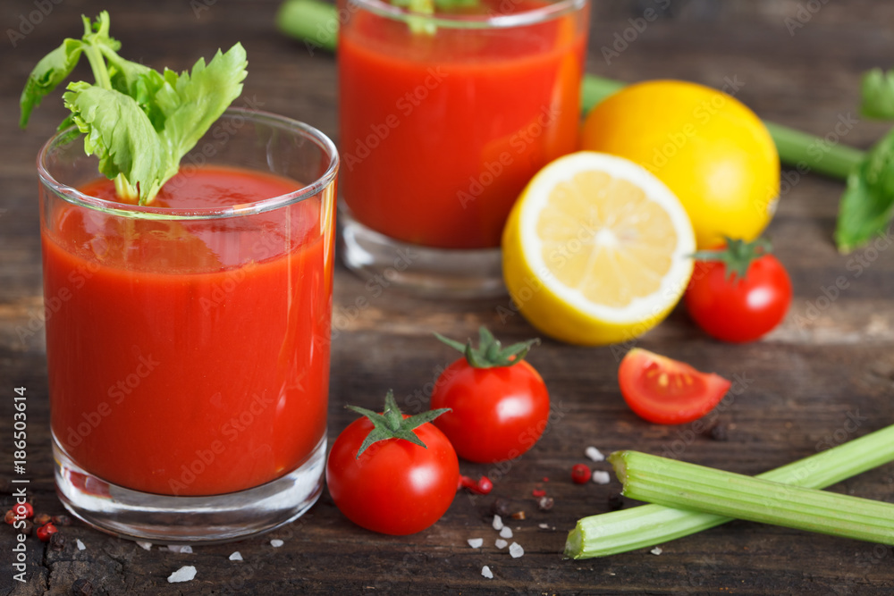 Glasses of tomato juice with cherry tomatoes, lemon and celery leaves on wooden table close up Glasses of tomato juice with cherry tomatoes, lemon and celery leaves on wooden table close up