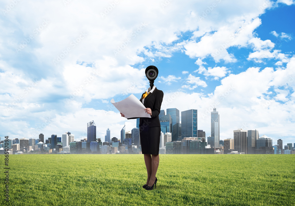 Camera headed woman standing on green grass against modern cityscape