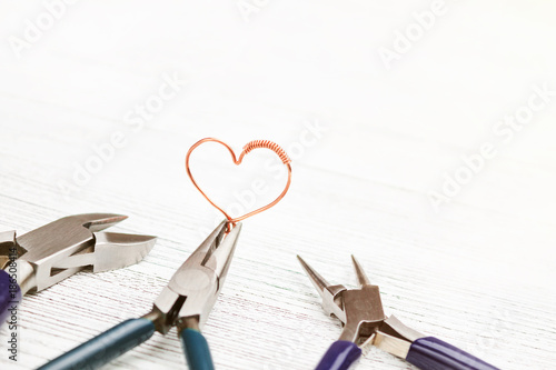 Jewelry tools on white background. Heart made of copper wire. Wire wrap photo