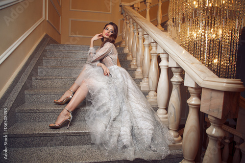 Fotografia, Obraz Full lenght portrait of gorgeous woman in the long silver dress on stairs