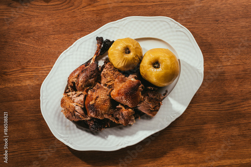 top view of fried duck pieces laying on plate with marinated apples over wooden table