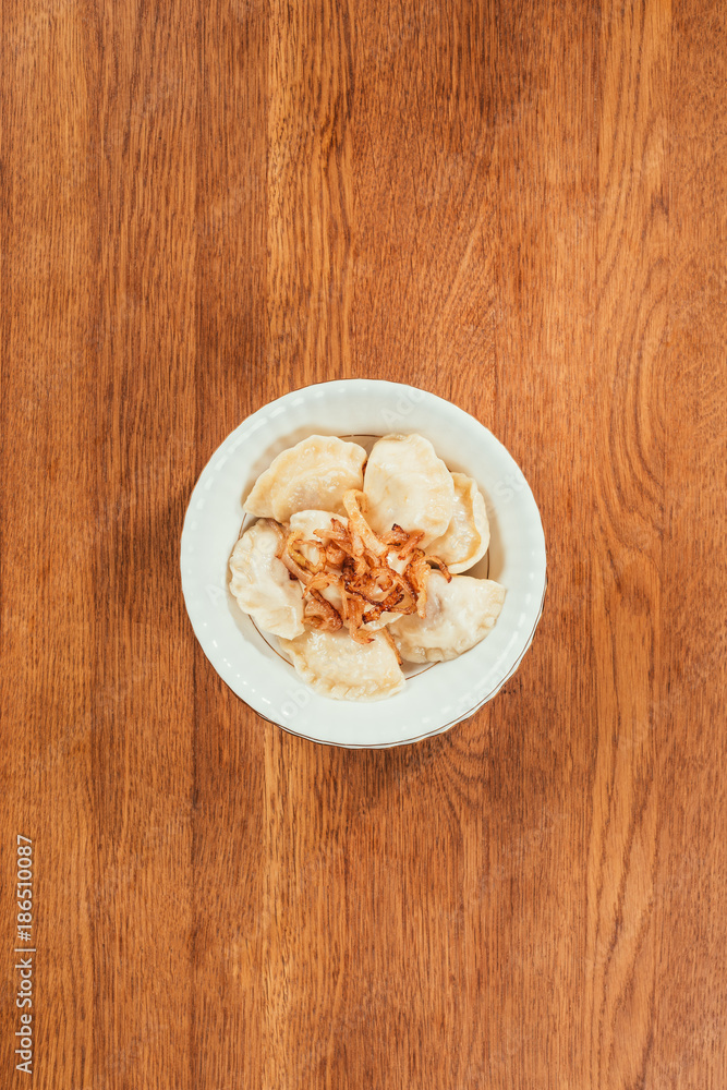 dumplings with fried onions on top laying in plate over wooden surface dumplings with fried onions on top laying in plate over wooden surface