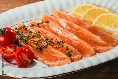 Close-up view of Salmon fish pieces with lemon, herbs and tomatoes on white plate