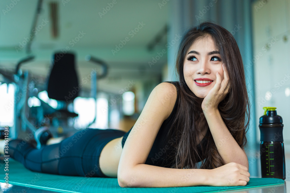 Sports woman lying and relaxing on yoga mat in fitness gym with sports  equipment background. Beauty and Workout training exercise concept. Body  build up and Strength theme. Stock Photo | Adobe Stock