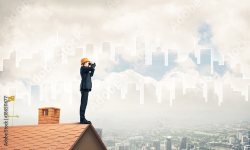 Engineer man standing on roof and looking in binoculars. Mixed m