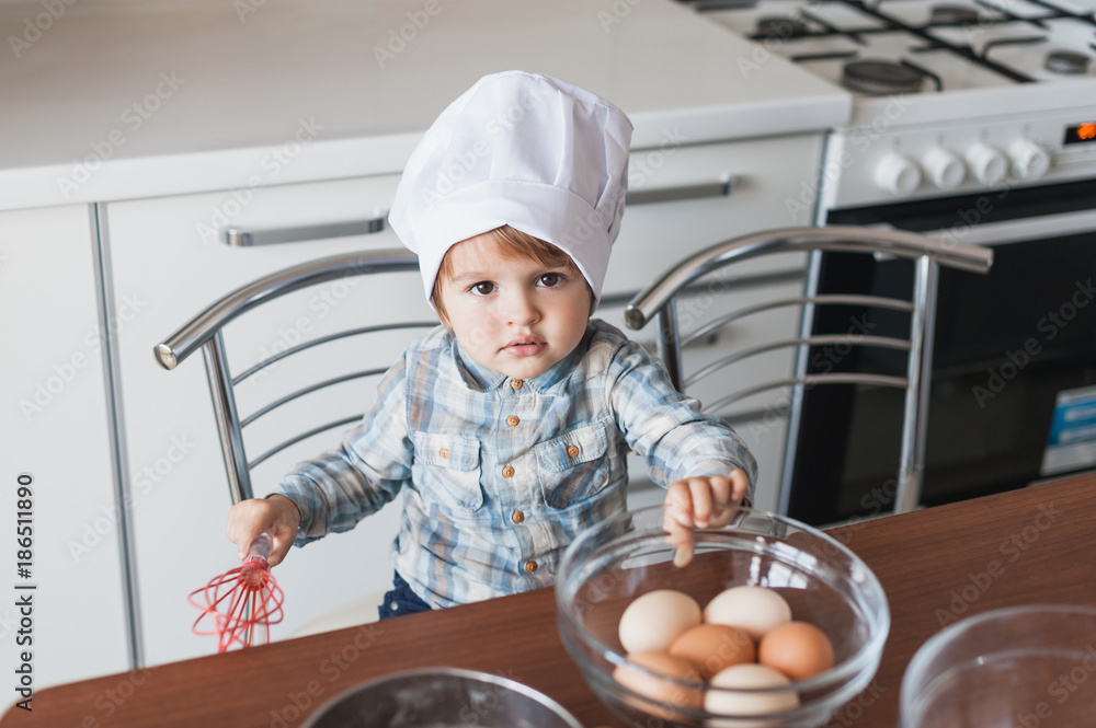 adorable little kid in chef hat with whisk and eggs in bowl