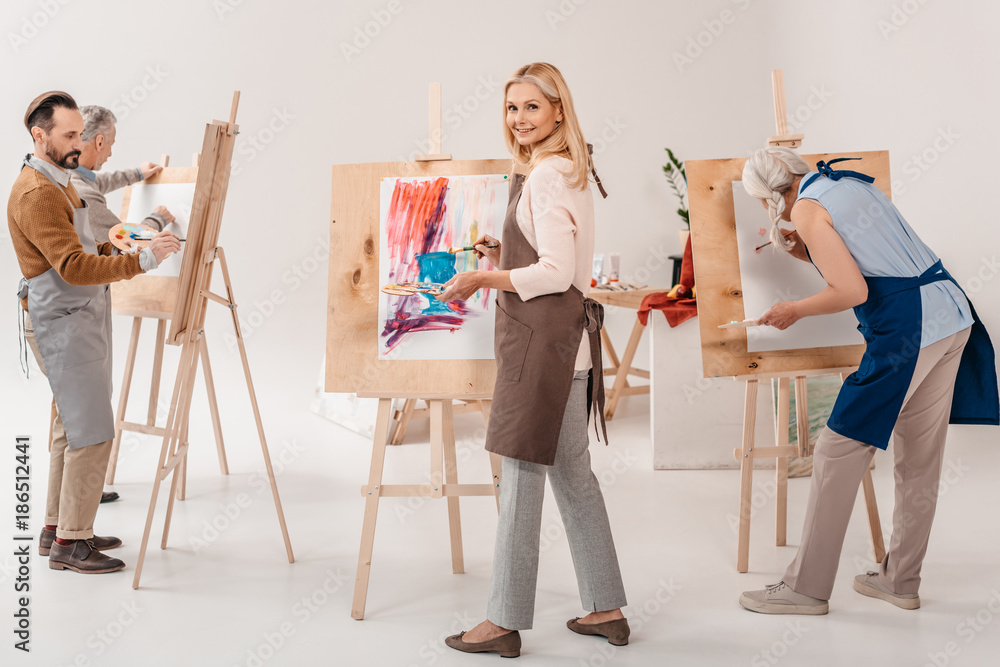 Naklejka premium male and female adult students in aprons painting together on easels in art class
