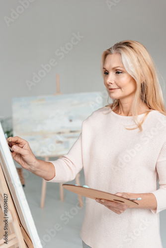 beautiful mature female artist painting on easel in art studio