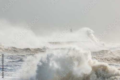 Newhaven, Sussex, Stormy Seas With Waves Crashing against Sea Wall. Lighthouse Partially Visible Behind. Wave Breaking in Foreground