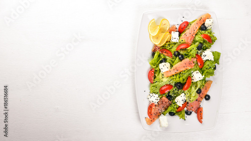 Salmon salad, feta cheese, salad leaves and fresh vegetables on the plate. On a wooden background. Top view. Free space for text.