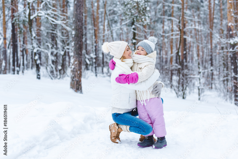 smiling daughter and mother hugging each other in winter forest