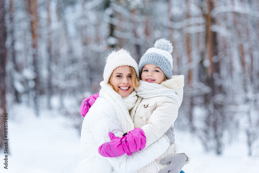 portrait of smiling daughter and mother hugging each other in winter forest