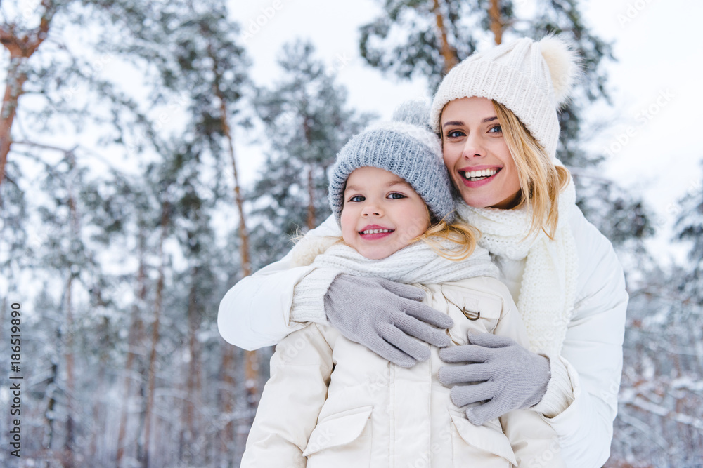 portrait of smiling mother hugging daughter while standing in winter park