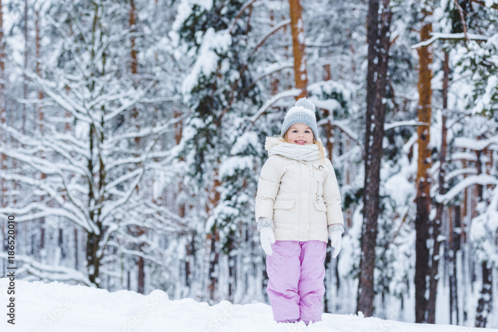 cheerful kid looking at camera while standing in winter forest