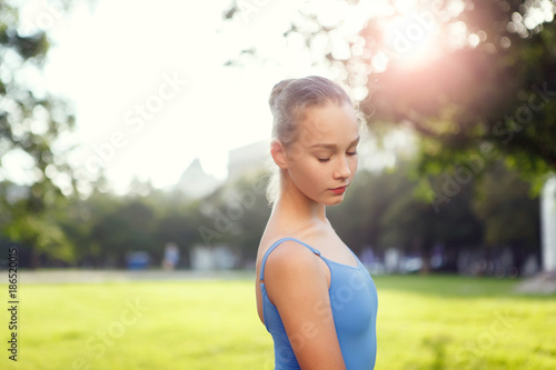 Fototapeta Naklejka Na Ścianę i Meble -  Young girl in blue sportwear half-length portrait in the park in sunny day. Portrait of ballet dancer dancing outdoor. Portrait of young lovely pretty beautiful girl in the park.