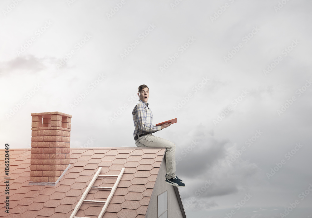 Handsome man on brick roof against cloud scape reading book Handsome man on brick roof against cloud scape reading book