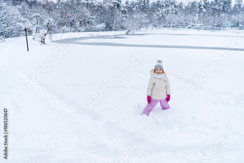 adorable happy child standing in snow and smiling at camera in winter park