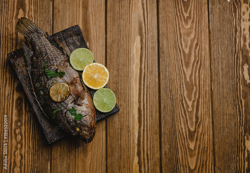 Top view baked fish with lemon and herbs on wooden board