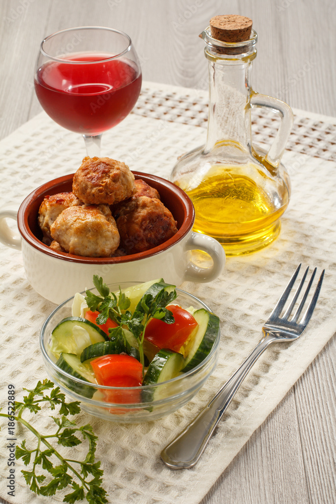 Fried meat cutlets in ceramic soup bowl, glass of wine, bottle with sunflower oil and salad of fresh cucumbers and tomatoes in glass bowl on white kitchen towel Fried meat cutlets in ceramic soup bowl, glass of wine, bottle with sunflower oil and salad of fresh cucumbers and tomatoes in glass bowl on white kitchen towel