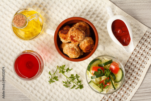 Fried meat cutlets in ceramic soup bowl, tomatoes, ceramic sauce boat with tomato sauce, branch of fresh parsley, glass of wine, kitchen towel and glass bottle with sunflower oil on grey wooden boards