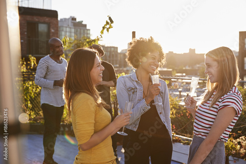 Female friends talking at a rooftop party, backlit photo