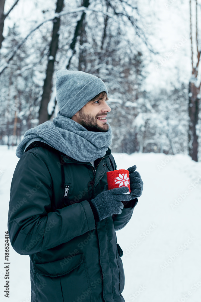 young man holding cup of hot coffee in hands in winter park