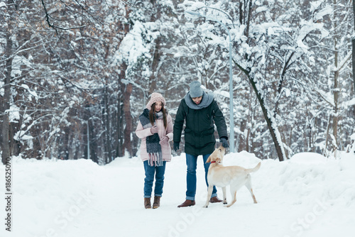 young couple having fun together with dog in winter park
