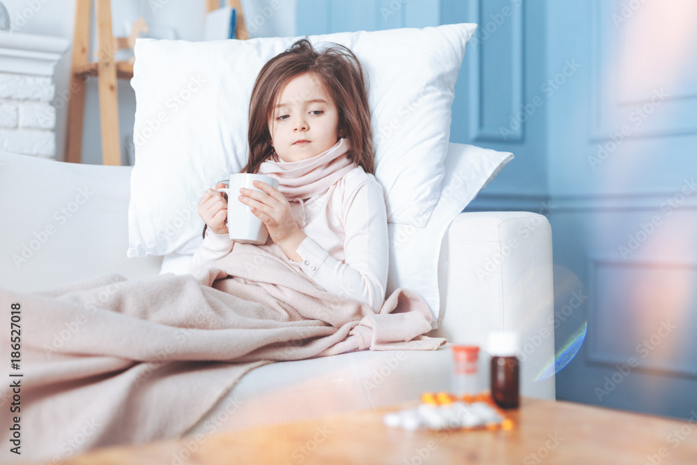 Deep in thoughts. Upset female person pressing her lips and looking aside while being in her bed with cup of tea Deep in thoughts. Upset female person pressing her lips and looking aside while being in her bed with cup of tea