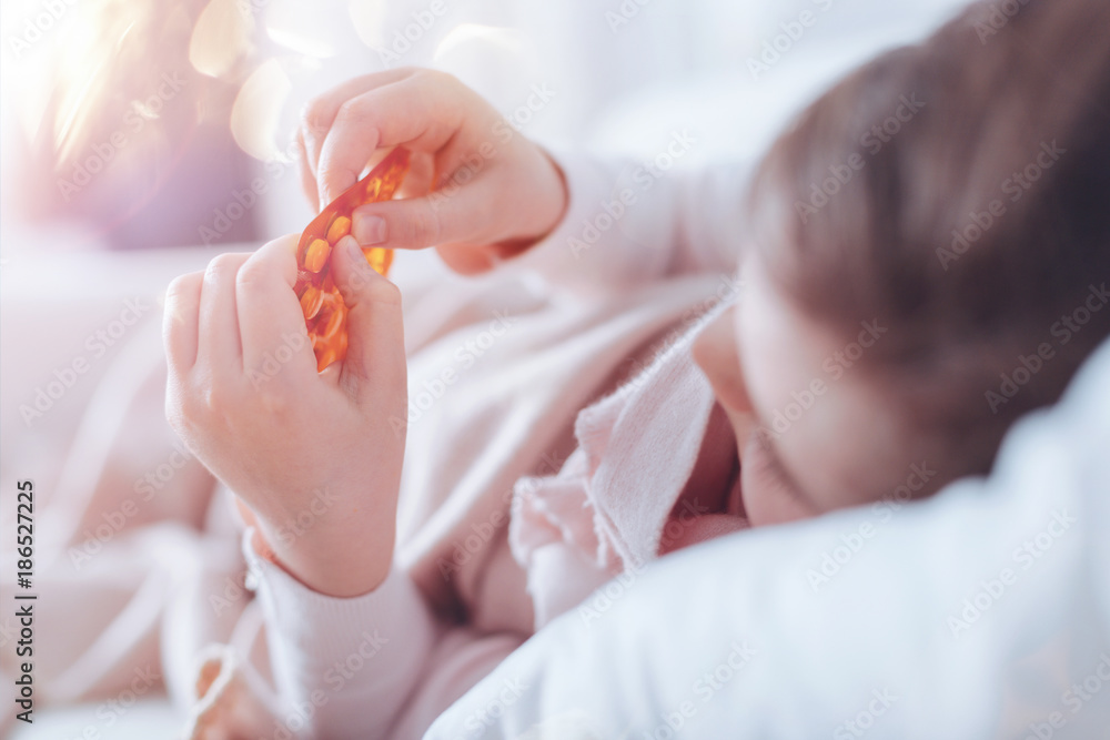 Taking pills. Little girl feeling unwell and lying in her bed while looking at her hands Taking pills. Little girl feeling unwell and lying in her bed while looking at her hands