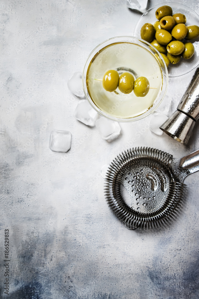 Classic alcoholic cocktail with dry vermouth and green olives, bar tools, gray background, top view Classic alcoholic cocktail with dry vermouth and green olives, bar tools, gray background, top view