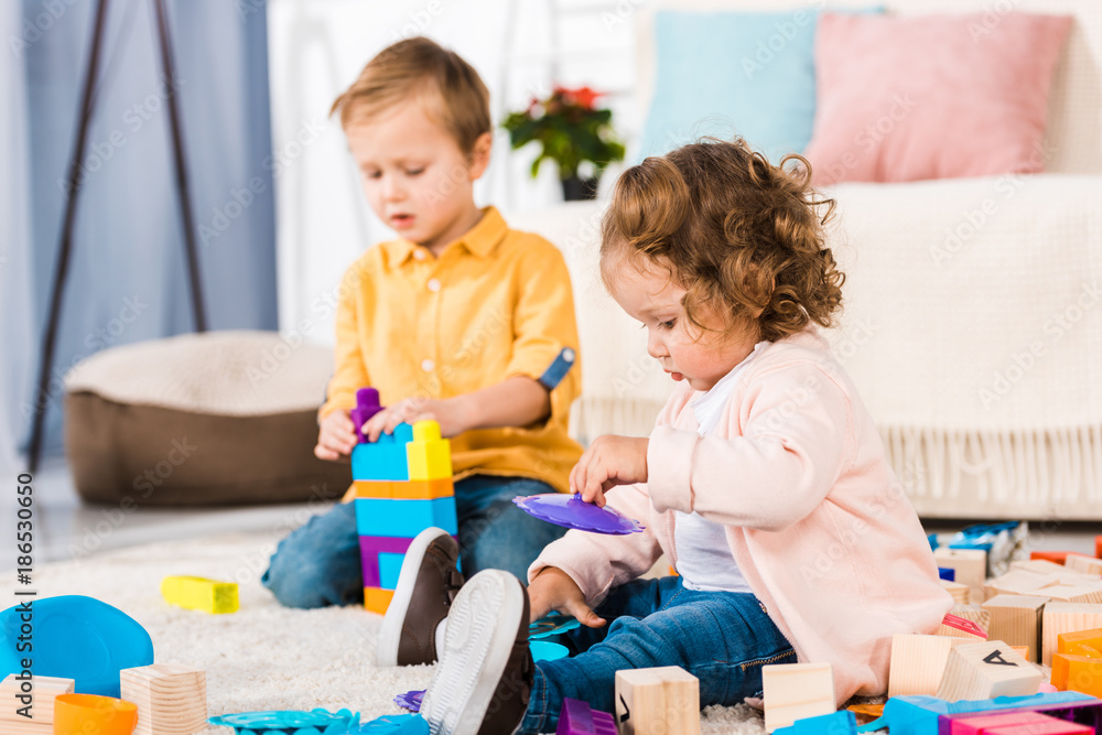 adorable siblings playing on a floor with plastic blocks adorable siblings playing on a floor with plastic blocks