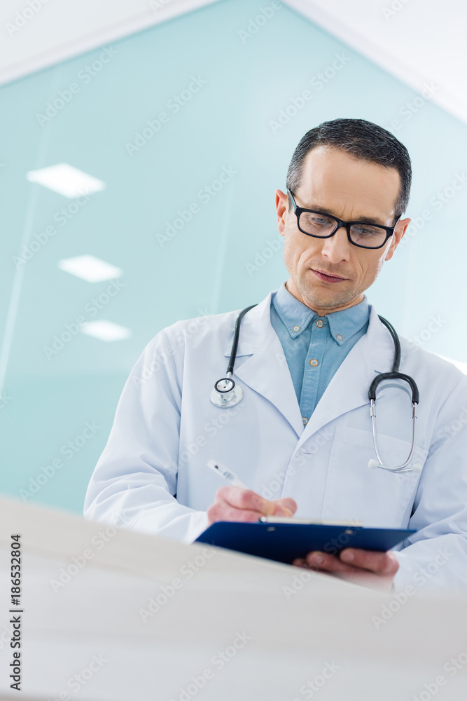 confident doctor in white coat with stethoscope writing diagnosis in hospital confident doctor in white coat with stethoscope writing diagnosis in hospital