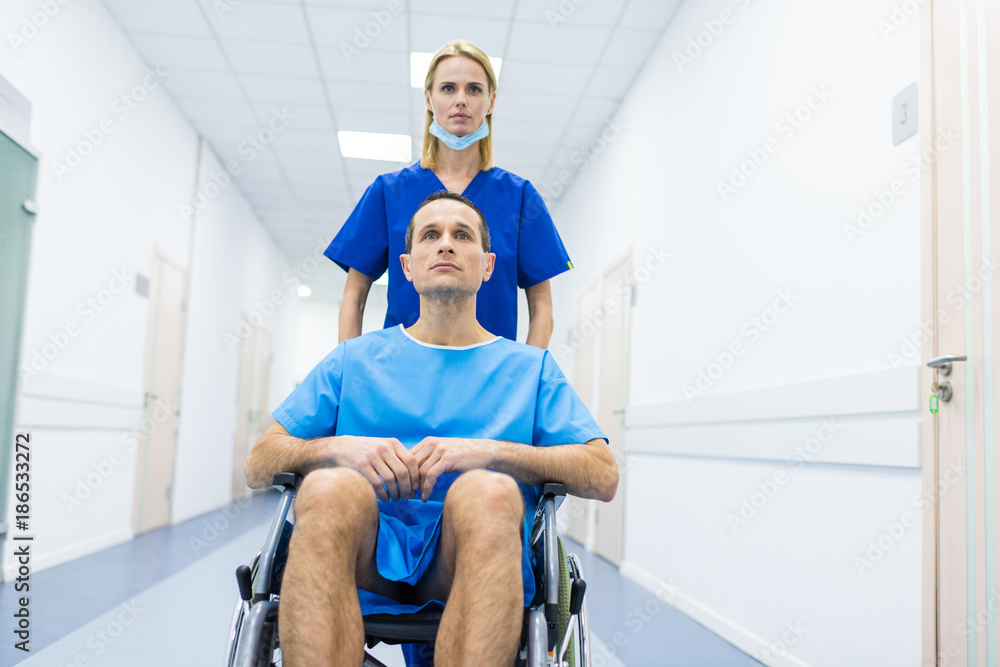 female surgeon and male patient in wheelchair in hospital corridor female surgeon and male patient in wheelchair in hospital corridor