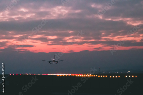A passenger or cargo plane lands on the runway against the background of red sunset