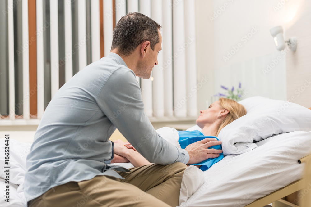 husband sitting at sick wife bed in hospital husband sitting at sick wife bed in hospital