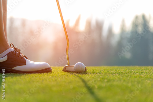 Golfer asian woman putting golf ball on the green golf on sun set evening time.  Healthy and Lifestyle Concept. photo