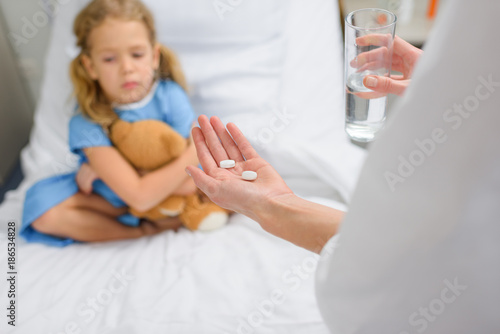 cropped image of doctor holding pills and water for child patient