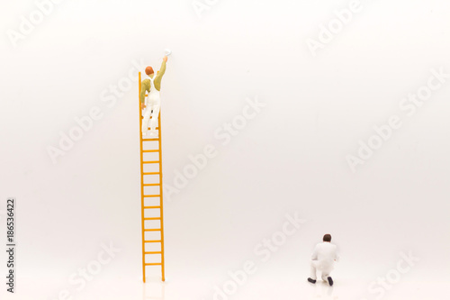 miniature people, mini figure with ladder and white paint in front of a wall and another one paint on bottom of wall. photo