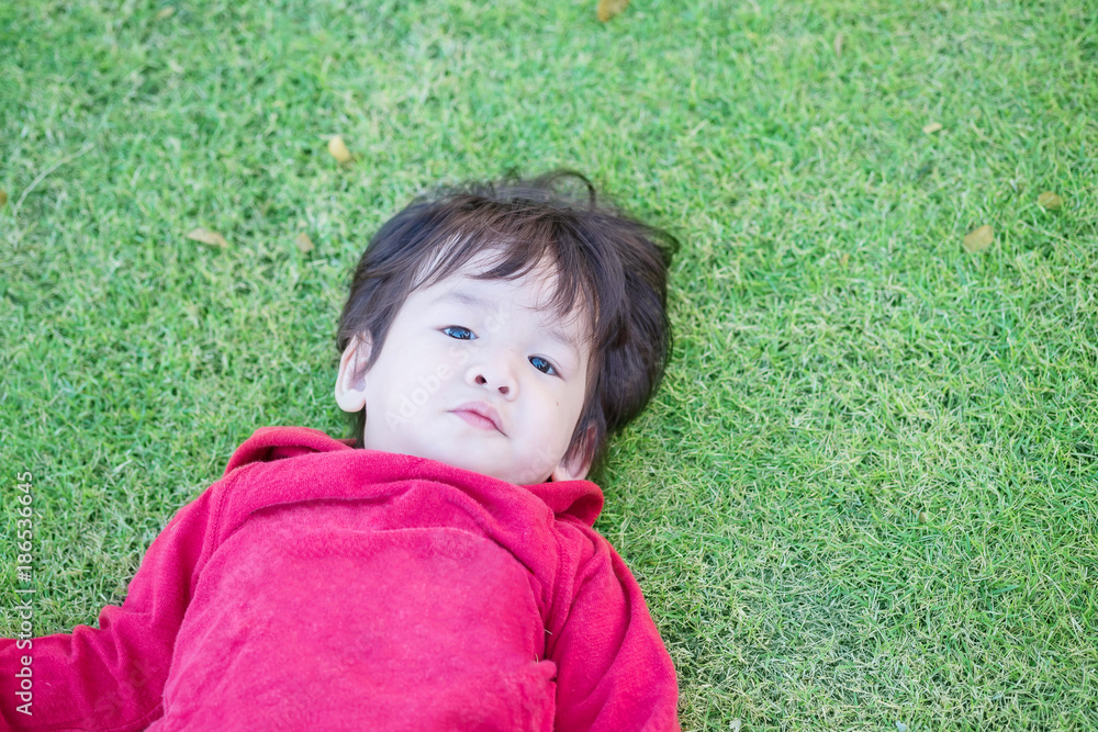 Closeup cute asian kid lie on grass floor in park textured background with copy space Closeup cute asian kid lie on grass floor in park textured background with copy space