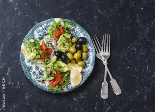 Mediterranean style antipasto plate. Smoked salmon, avocado, arugula bruschetta, olives and grapes on dark background