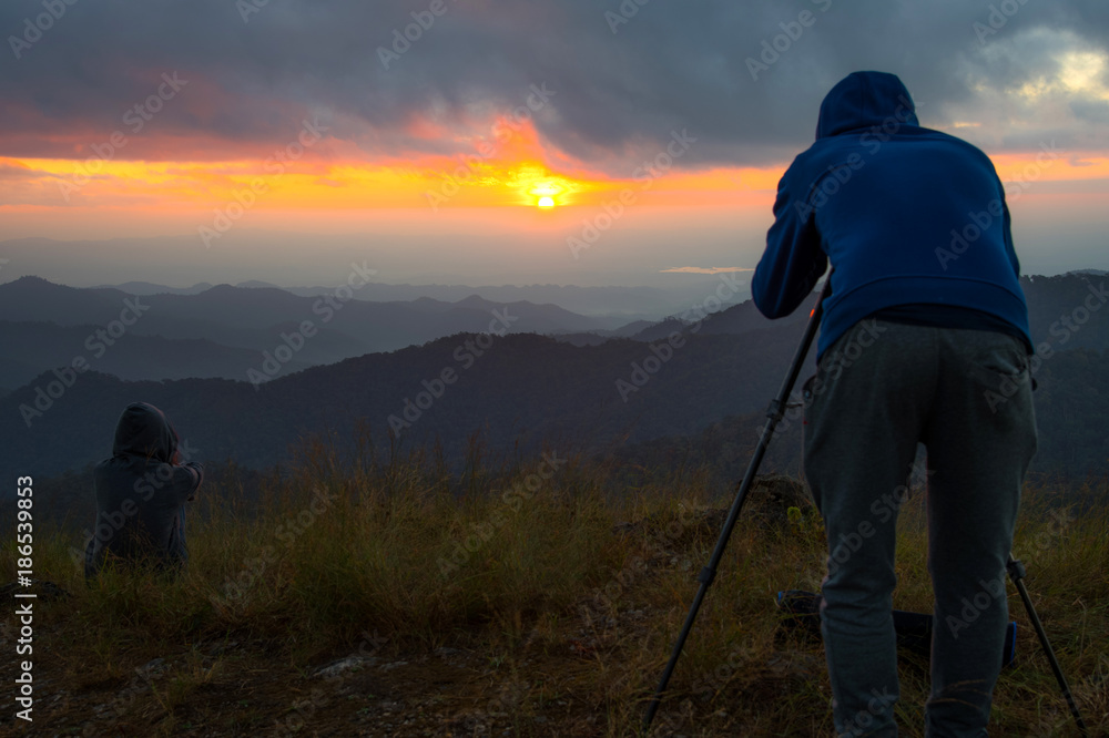 Travel photographer man taking nature photo of mountain landscape and girl sitting to see view sunset on mountain. Hiker tourist photographer on adventure vacation shooting slr camera on tripod Travel photographer man taking nature photo of mountain landscape and girl sitting to see view sunset on mountain. Hiker tourist photographer on adventure vacation shooting slr camera on tripod
