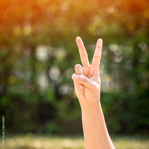 Women show hands with victory sign on bokeh background in public park. © Watchara