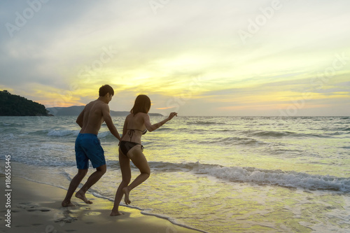 Asian couple holding hand together and running on beach to the sea with bikini and evening light. Relax and traveling at sea concpet.