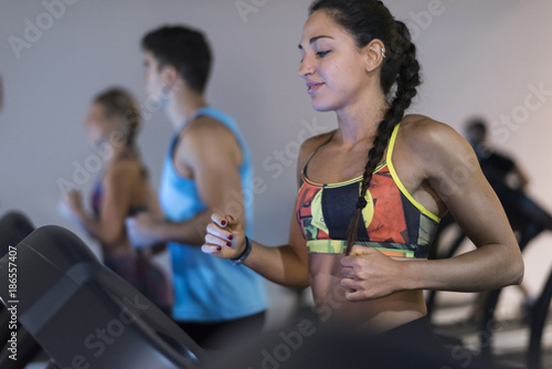 People running in treadmill in gym, young woman with braided hair training