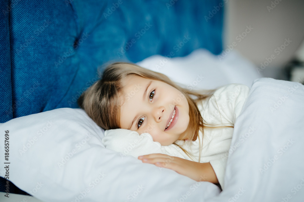 Sweet little girl before sleeping or wake up with smile in her bed at home, close up Sweet little girl before sleeping or wake up with smile in her bed at home, close up