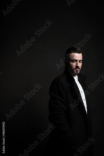 Portrait of a stylish young man in a black coat. Black background.